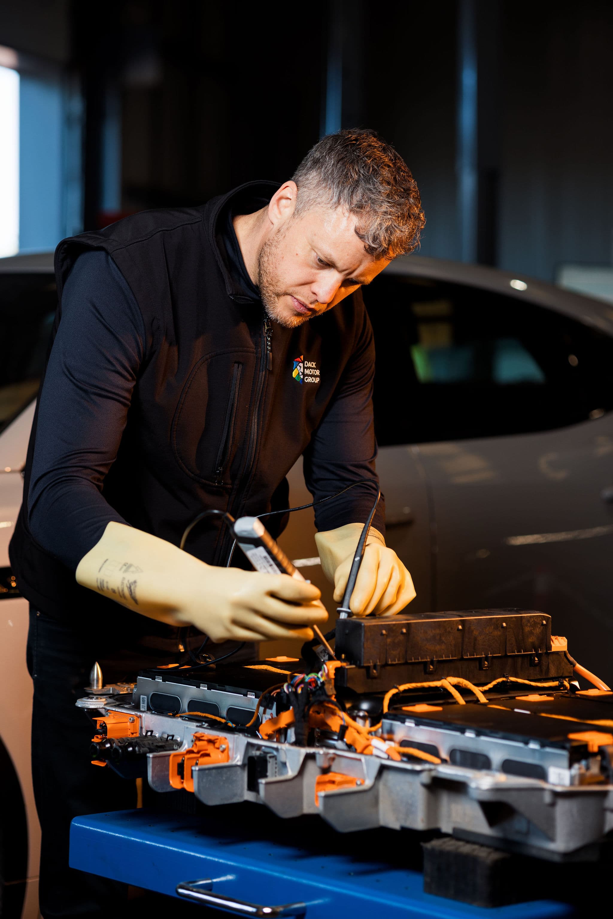 Dack technician in insulated high-voltage gloves testing an electric vehicle battery pack